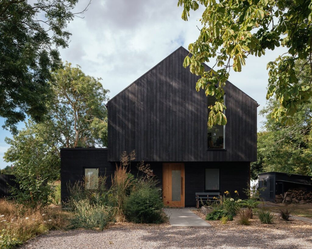 a black house with a gravel driveway and trees